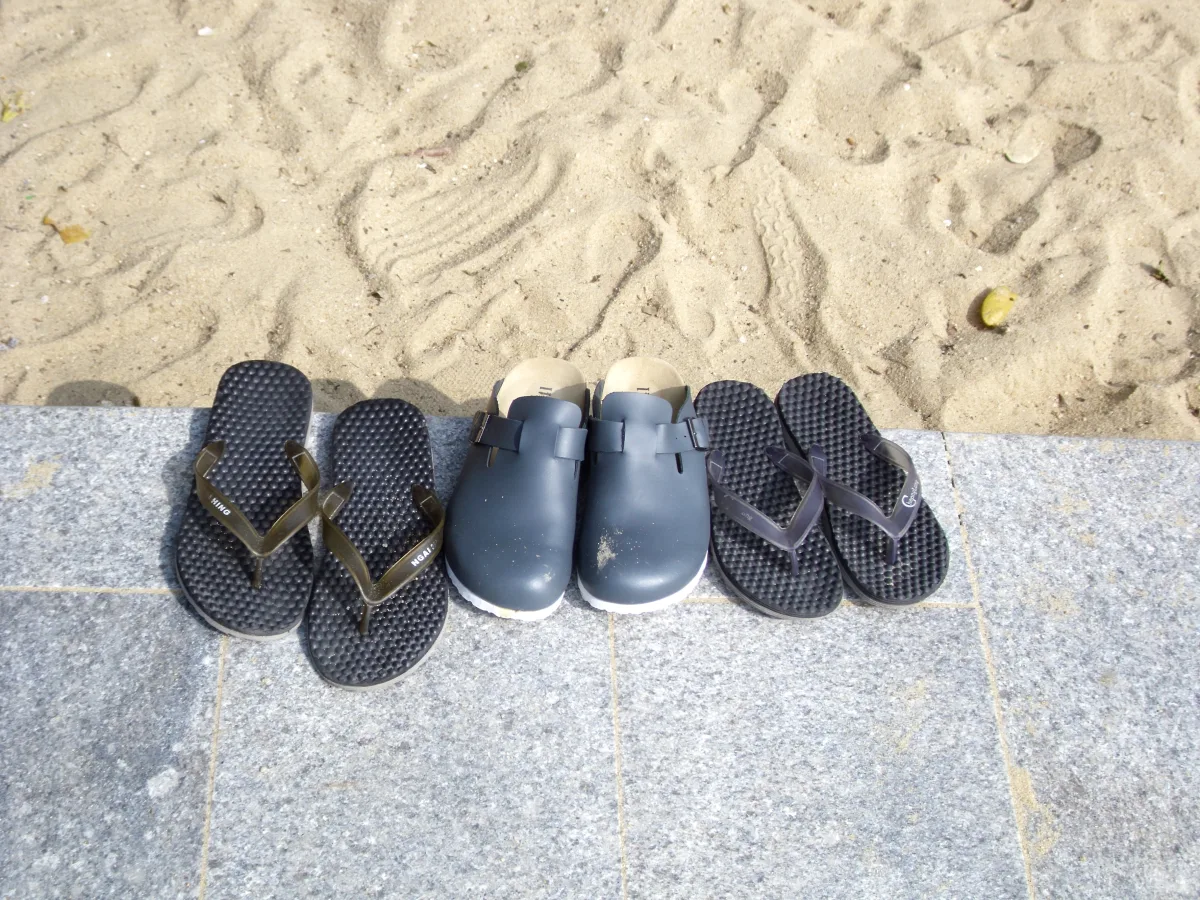 Un par de chanclas negras y unas sandalias de cuero sobre la arena de la playa