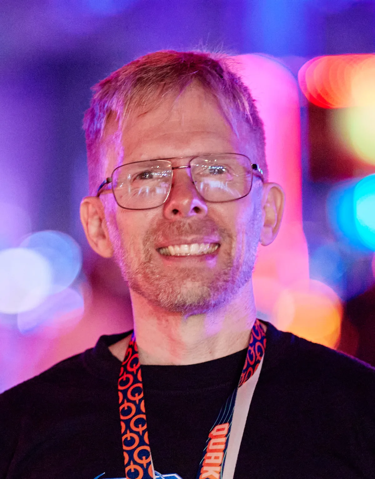 John Carmack, con gafas y camiseta negra, entre luces de colores en un congreso