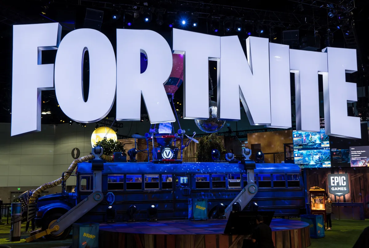 El rótulo gigante de FORTNITE iluminado sobre el autobús de batalla, montado como escenario en una feria de videojuegos