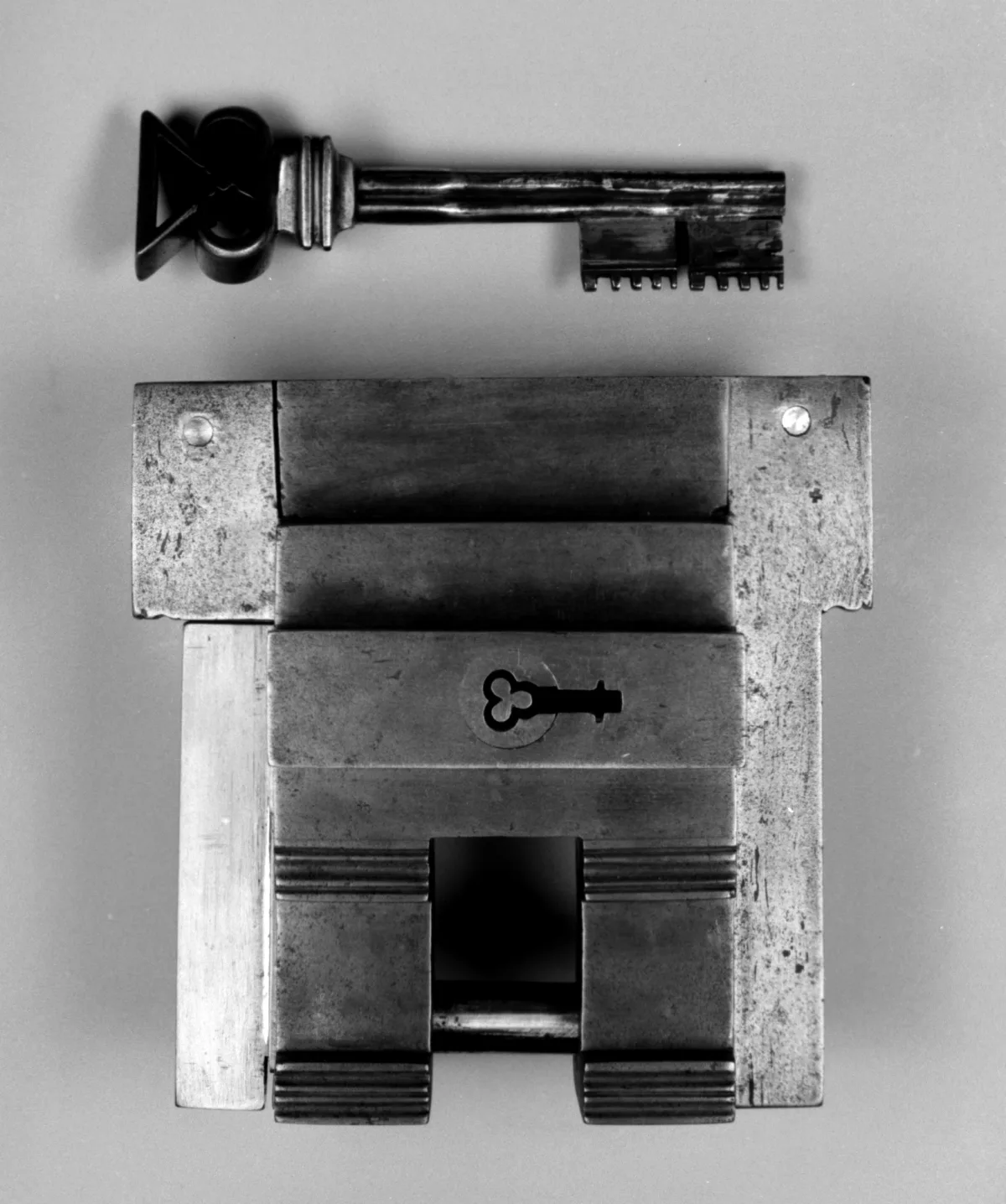Un candado de hierro antiguo fotografiado sobre fondo gris, con su llave colocada justo encima