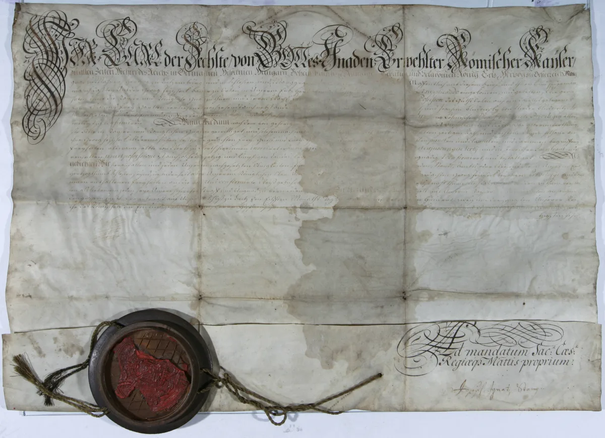 Pergamino manuscrito con caligrafía gótica y, colgando del borde inferior mediante un cordón de seda, un gran sello de cera roja dentro de una caja de madera