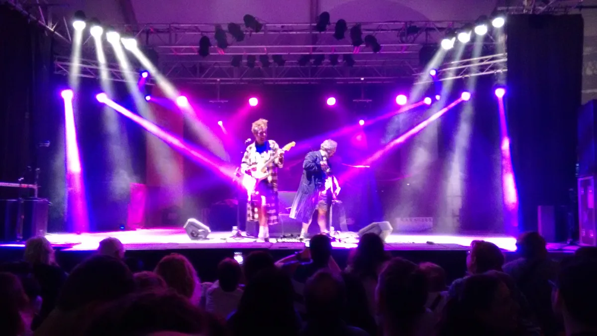 Los Gandules tocando sobre un escenario iluminado de morado, con el público de espaldas en primer plano