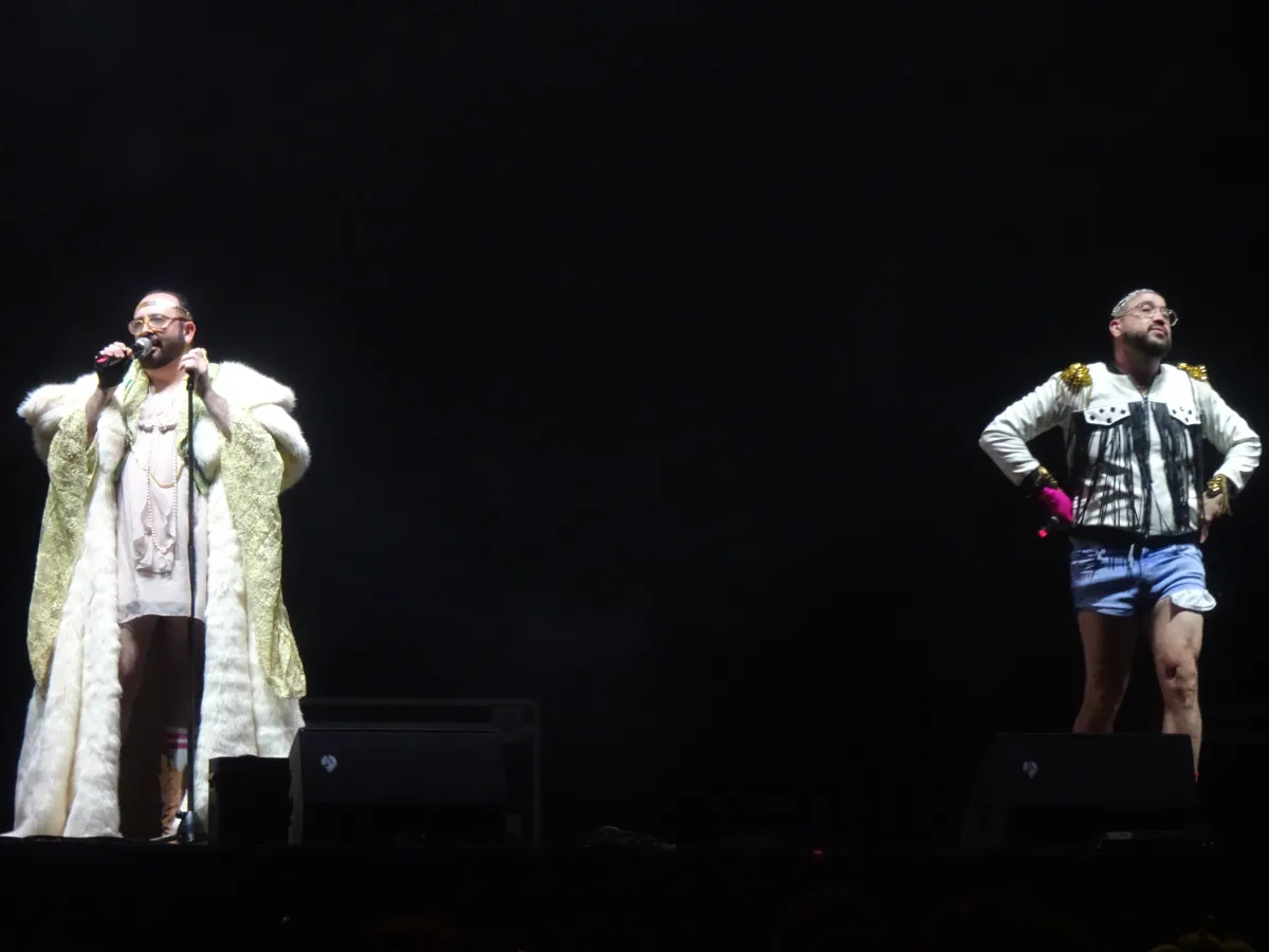 Los dos miembros de Ojete Calor cantando en un escenario a oscuras, con vestuario estrafalario