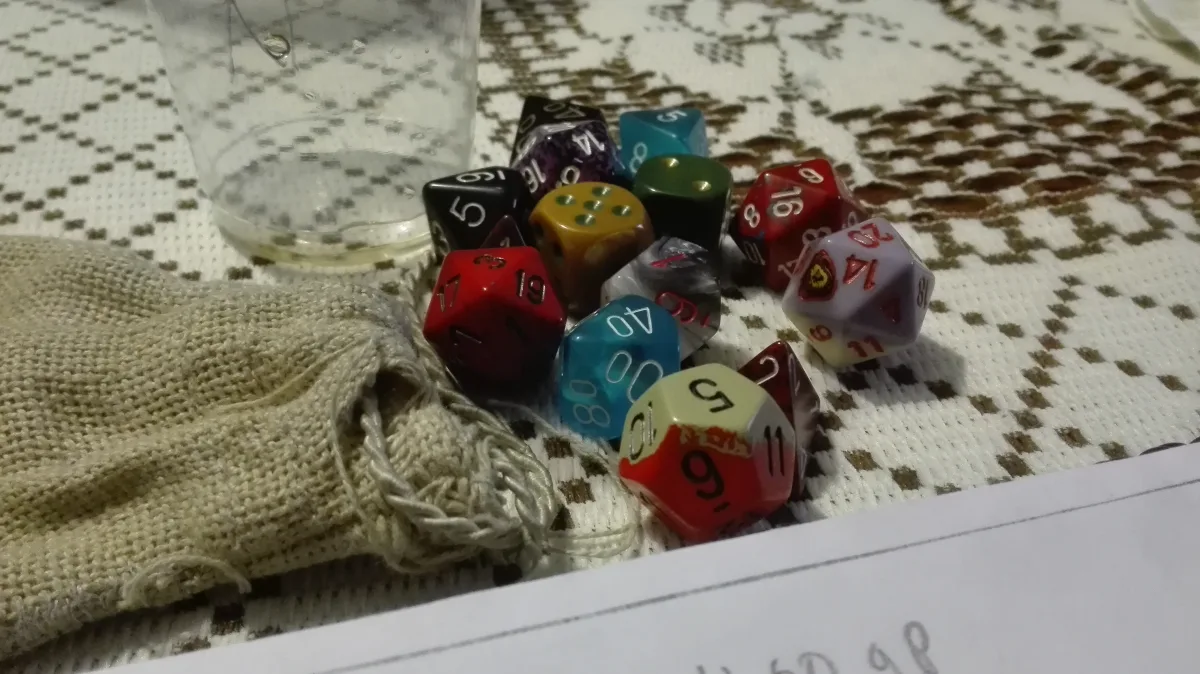 Dados poliédricos de colores saliendo de una bolsa de tela sobre la mesa, junto a una hoja de personaje