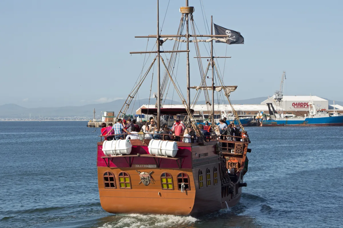Una bandera pirata negra con la calavera y las tibias ondeando sobre un barco
