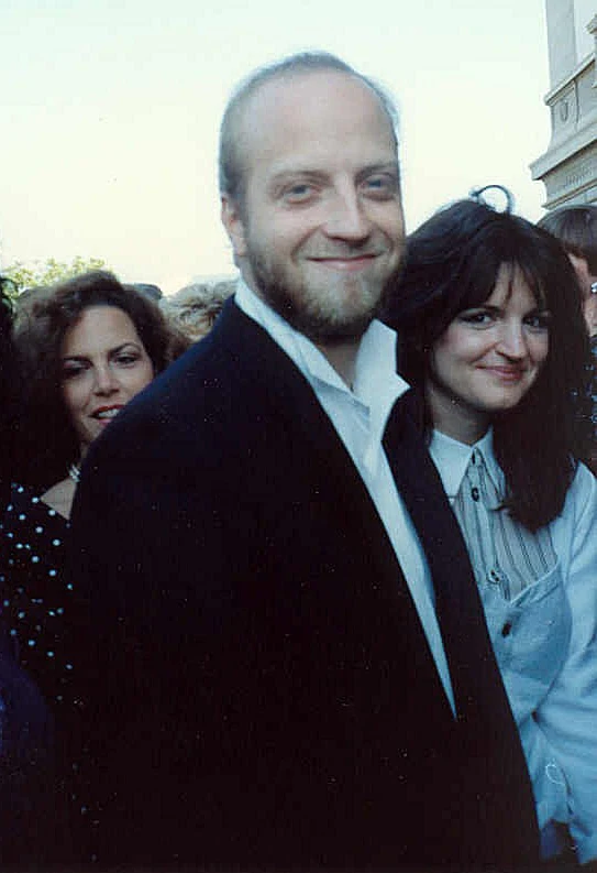 Chris Elliott, con barba y traje oscuro, sonriendo entre la gente en una alfombra roja