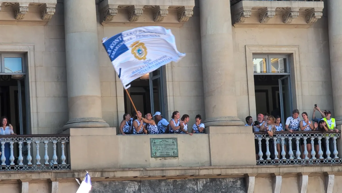 Remeras de Arraun Lagunak, con camisetas blancas con manchas azules, ondeando desde el balcón del antiguo Ayuntamiento de la plaza de la Constitución la bandera de la XIX Kontxako Bandera femenina de 2026