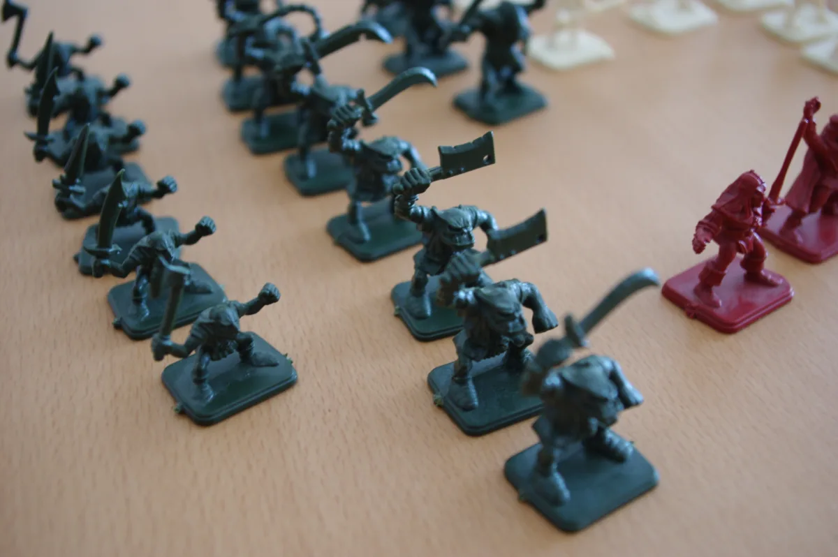Filas de miniaturas verdes de plástico de HeroQuest sobre una mesa, con dos figuras rojas al lado