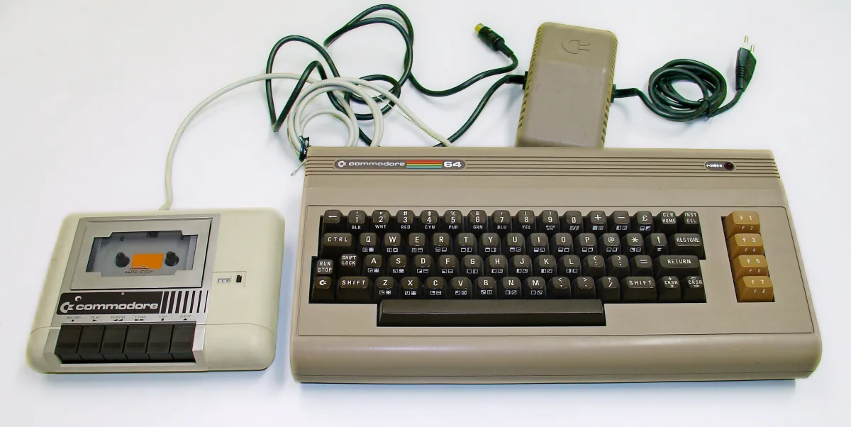 Un Commodore 64 beis con su teclado y, a la izquierda, la unidad de casete Datasette con una cinta dentro